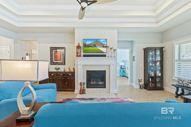 living room featuring crown molding, ceiling fan, a tile fireplace, and a raised ceiling