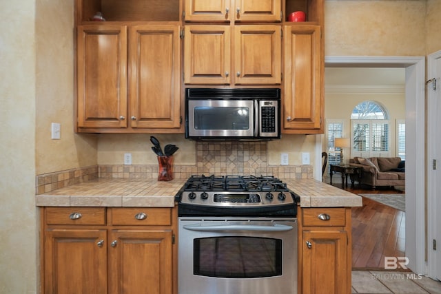 kitchen with stainless steel appliances, ornamental molding, tile countertops, and tasteful backsplash