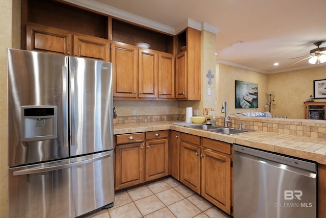 kitchen featuring appliances with stainless steel finishes, tile counters, sink, ornamental molding, and light tile patterned floors