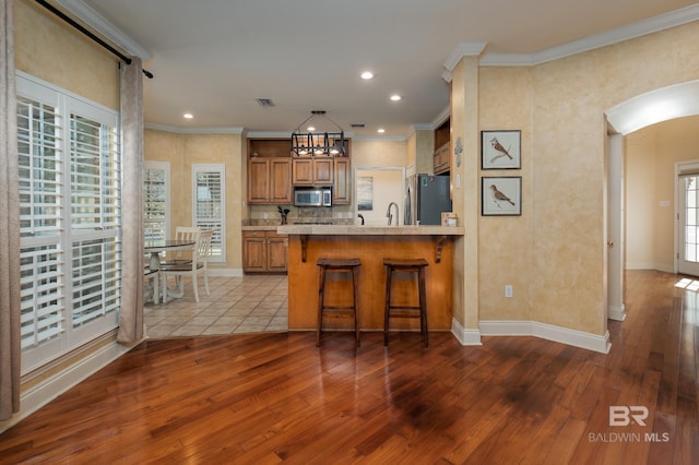 kitchen with stainless steel appliances, kitchen peninsula, hardwood / wood-style flooring, a breakfast bar, and crown molding