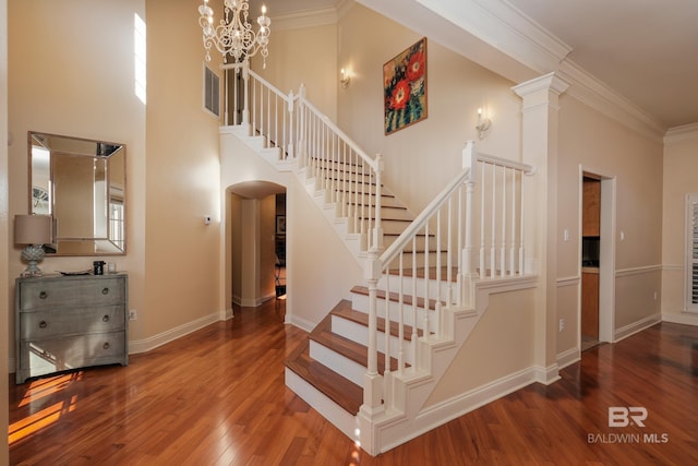 staircase with crown molding, hardwood / wood-style floors, decorative columns, a chandelier, and a high ceiling