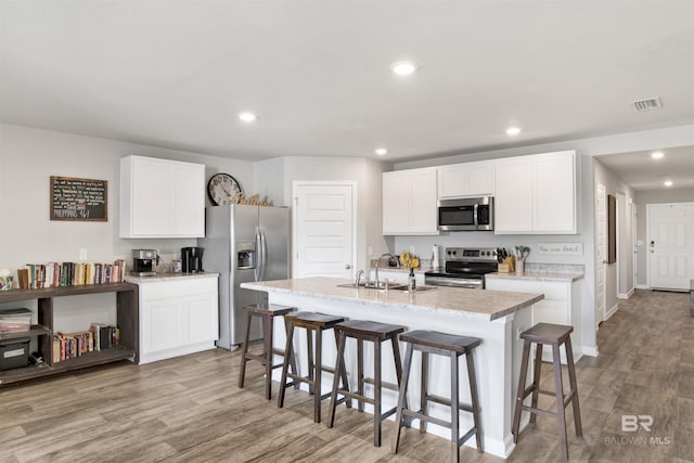 kitchen featuring sink, a center island with sink, stainless steel appliances, light hardwood / wood-style floors, and white cabinets