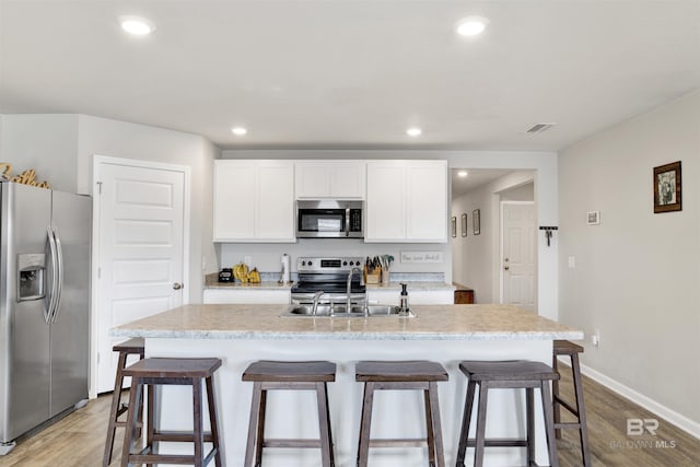 kitchen featuring sink, stainless steel appliances, white cabinets, and a center island with sink