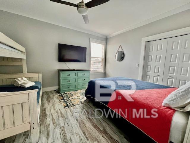 bedroom with ceiling fan, wood-type flooring, crown molding, and a closet