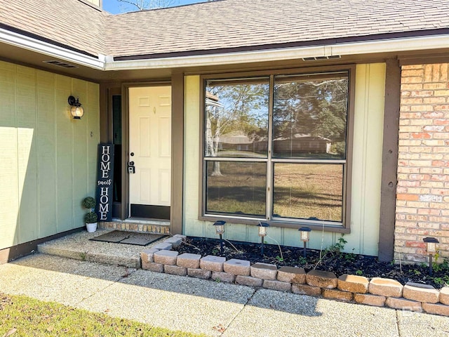 doorway to property featuring brick siding and roof with shingles