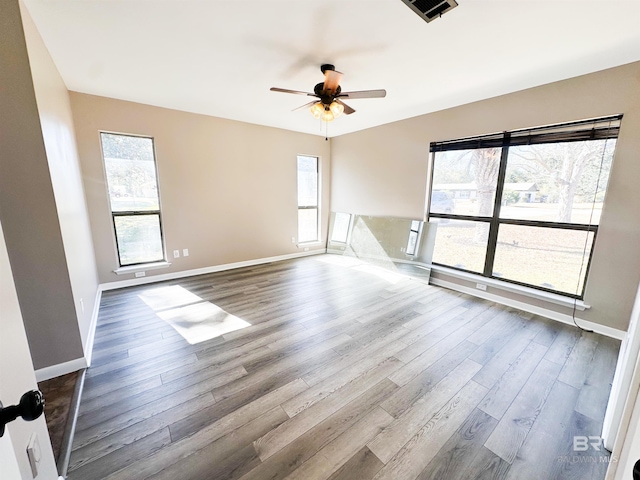 unfurnished room with a ceiling fan, wood finished floors, visible vents, and baseboards