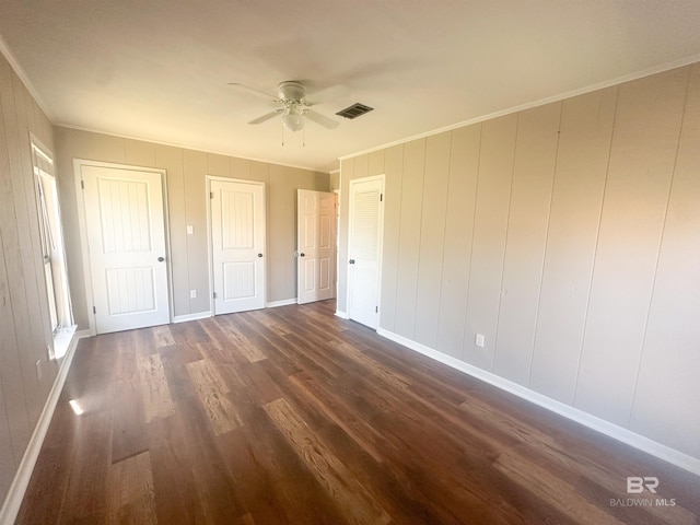 unfurnished bedroom with baseboards, visible vents, ornamental molding, dark wood-style flooring, and multiple closets