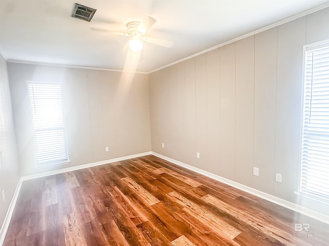 spare room featuring wood finished floors, a ceiling fan, a healthy amount of sunlight, visible vents, and crown molding