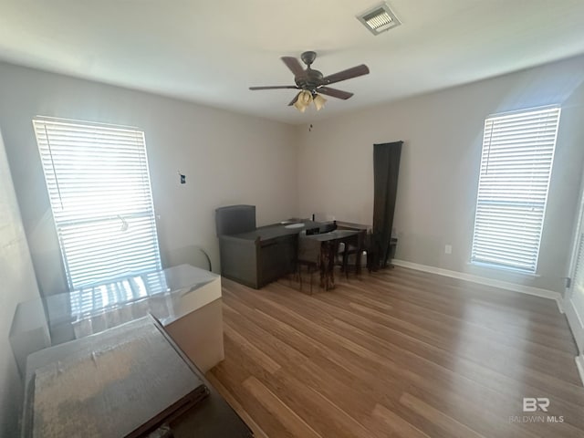 office featuring wood finished floors, visible vents, baseboards, a ceiling fan, and a wealth of natural light