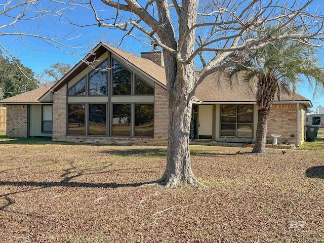 back of property featuring brick siding, a lawn, and roof with shingles