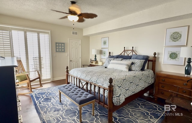 bedroom with a ceiling fan, a textured ceiling, visible vents, wood finished floors, and baseboards