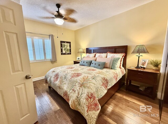 bedroom featuring baseboards, a ceiling fan, hardwood / wood-style flooring, and a textured ceiling