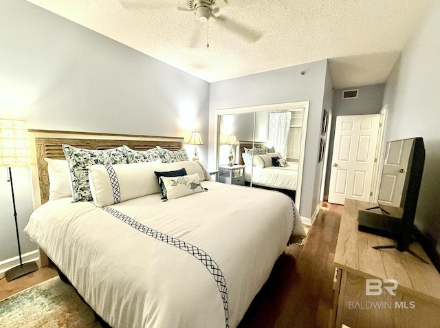 bedroom with visible vents, wood finished floors, baseboards, ceiling fan, and a textured ceiling