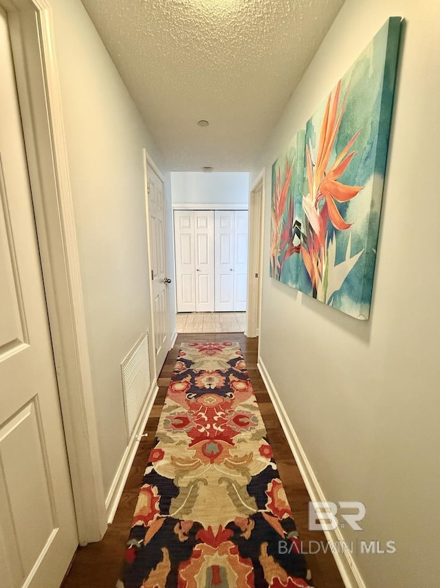 hallway with visible vents, a textured ceiling, dark wood finished floors, and baseboards