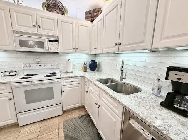 kitchen with white cabinets, light stone counters, a sink, white appliances, and decorative backsplash