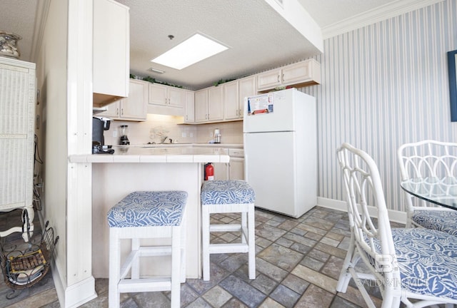 kitchen with a skylight, a kitchen breakfast bar, white cabinets, tile countertops, and white fridge