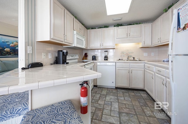 kitchen featuring tile counters, kitchen peninsula, white appliances, decorative backsplash, and white cabinets