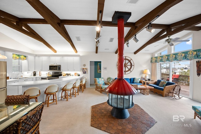 living room with light carpet, beamed ceiling, track lighting, and ceiling fan