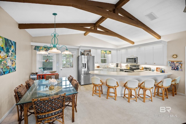 kitchen with lofted ceiling with beams, appliances with stainless steel finishes, hanging light fixtures, light countertops, and white cabinetry