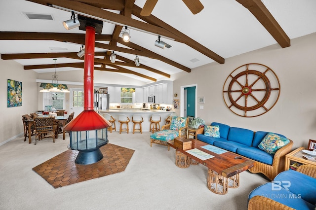 living area featuring ceiling fan, visible vents, a wood stove, and vaulted ceiling with beams