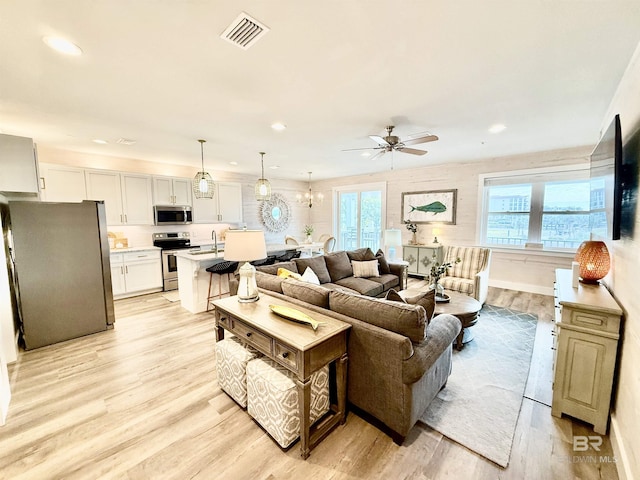 living room with ceiling fan with notable chandelier, sink, and light hardwood / wood-style flooring