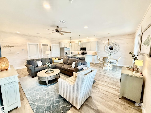 living room featuring ornamental molding, ceiling fan with notable chandelier, and light hardwood / wood-style flooring