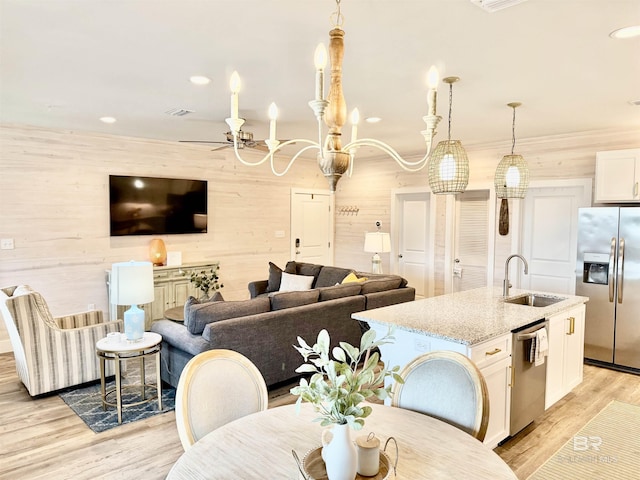 kitchen with sink, light stone counters, decorative light fixtures, appliances with stainless steel finishes, and wooden walls