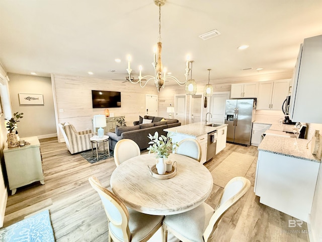 dining space with sink, light hardwood / wood-style flooring, a chandelier, and wood walls