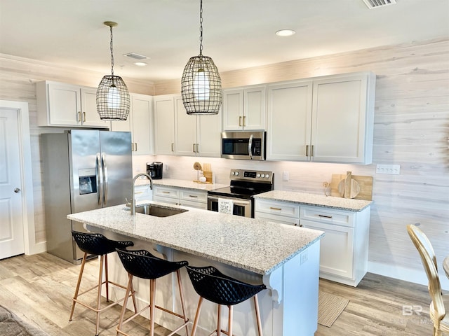 kitchen with sink, appliances with stainless steel finishes, light stone countertops, white cabinets, and decorative light fixtures