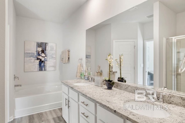 bathroom with a garden tub, wood finished floors, a stall shower, and a sink