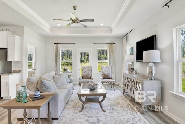 living room with light wood-type flooring, baseboards, ornamental molding, and a raised ceiling