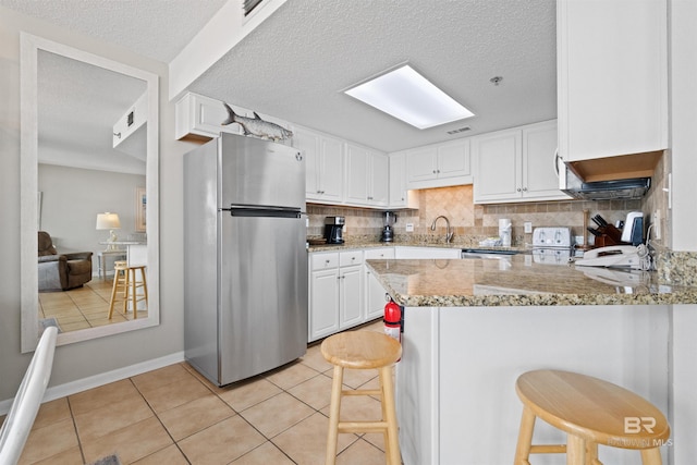 26802 Perdido Beach Blvd Unit 7C2, Orange Beach, AL 36561 - kitchen featuring freestanding refrigerator, a peninsula, light tile patterned flooring, white cabinets, and backsplash
