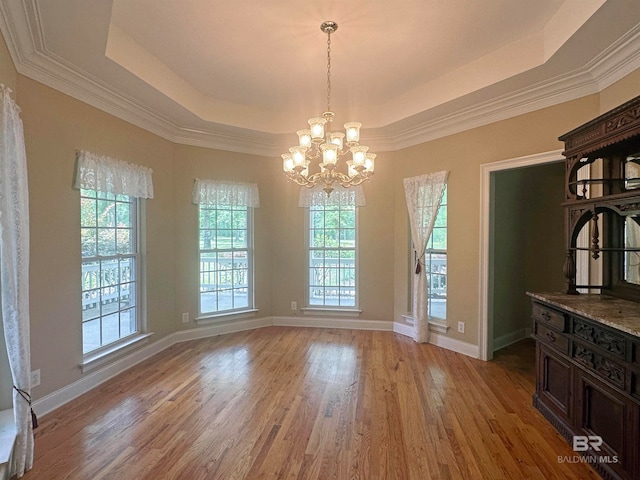 unfurnished dining area with crown molding, a notable chandelier, a tray ceiling, and hardwood / wood-style floors