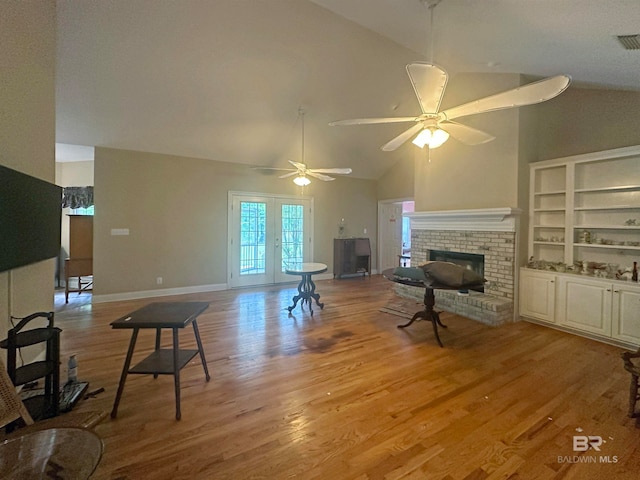 living room with light hardwood / wood-style floors, french doors, a brick fireplace, high vaulted ceiling, and ceiling fan