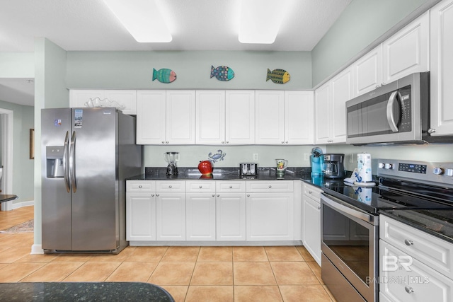 kitchen with light tile patterned flooring, dark stone counters, stainless steel appliances, and white cabinets