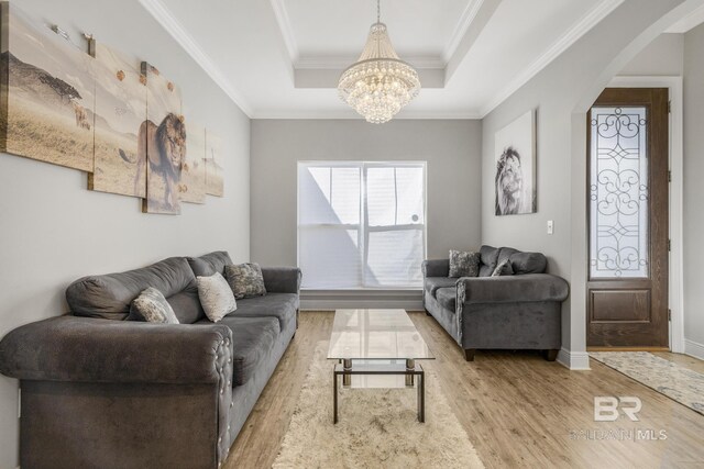living area with crown molding, arched walkways, wood finished floors, a raised ceiling, and a notable chandelier