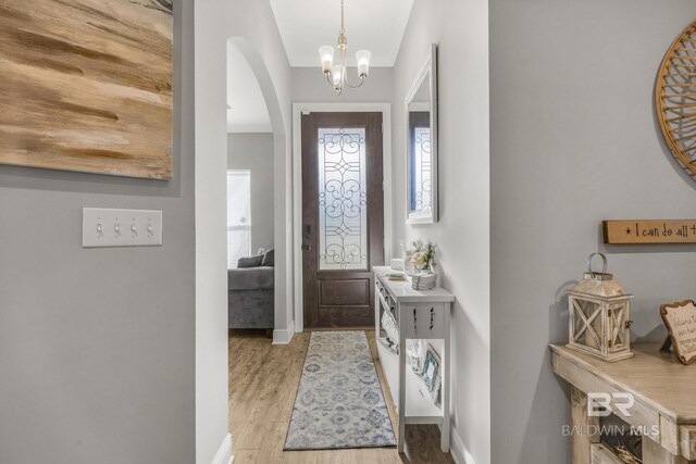 entrance foyer with a notable chandelier, light wood finished floors, arched walkways, baseboards, and ornamental molding