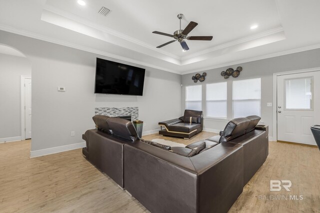 living room featuring a raised ceiling, light wood-style floors, arched walkways, a tiled fireplace, and a ceiling fan