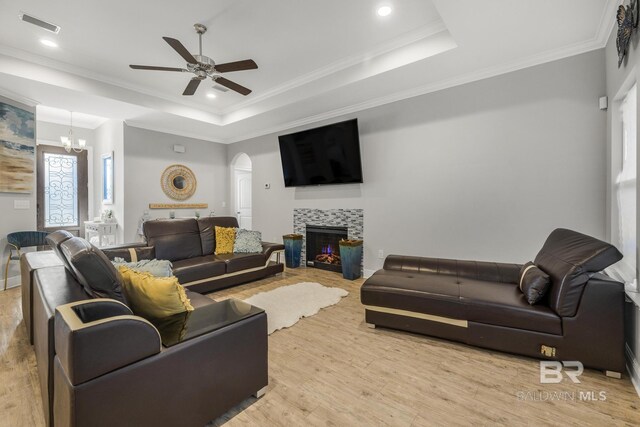 living area featuring visible vents, light wood-type flooring, a raised ceiling, arched walkways, and ceiling fan with notable chandelier