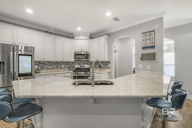 kitchen with a kitchen breakfast bar, arched walkways, wood finished floors, a sink, and stainless steel appliances