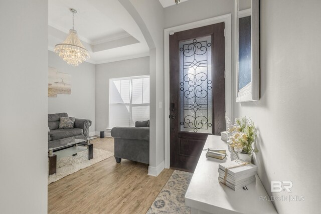 foyer entrance featuring an inviting chandelier, light wood-style floors, arched walkways, baseboards, and ornamental molding