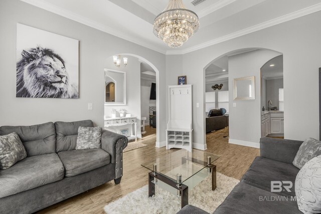 living area featuring crown molding, an inviting chandelier, arched walkways, baseboards, and light wood-type flooring