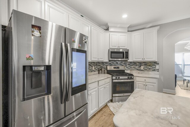 kitchen with arched walkways, light wood finished floors, white cabinets, and stainless steel appliances