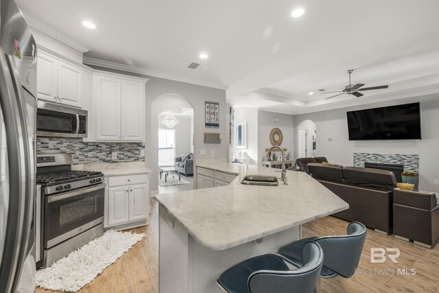 kitchen with a sink, ceiling fan, a kitchen bar, arched walkways, and appliances with stainless steel finishes