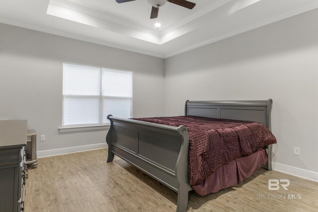 bedroom with a ceiling fan, crown molding, baseboards, light wood finished floors, and a tray ceiling