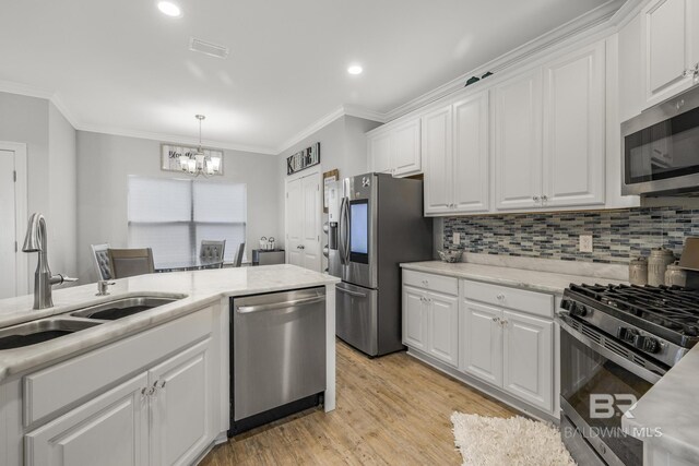 kitchen featuring appliances with stainless steel finishes, an inviting chandelier, a sink, white cabinetry, and ornamental molding