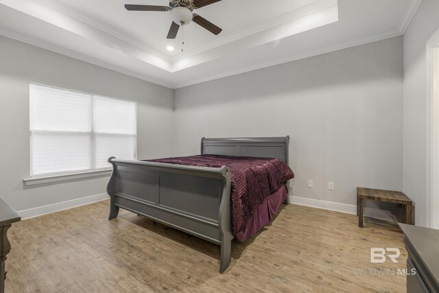 bedroom featuring crown molding, a raised ceiling, baseboards, and light wood-style flooring