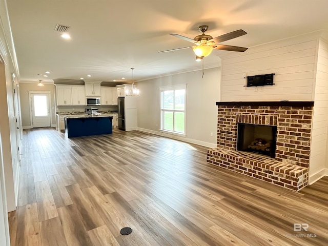 unfurnished living room featuring ceiling fan, crown molding, a brick fireplace, and light hardwood / wood-style floors