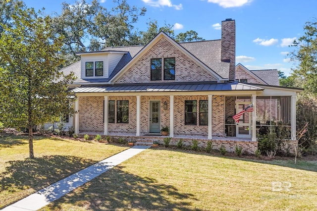 view of front of house featuring brick siding, a chimney, covered porch, a standing seam roof, and a front yard