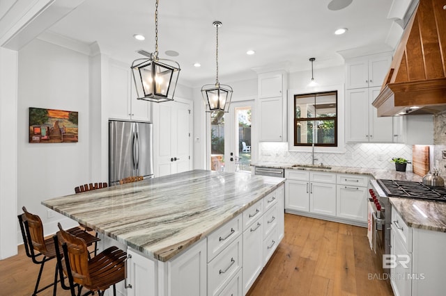 kitchen with stainless steel appliances, white cabinets, custom range hood, a center island, and pendant lighting